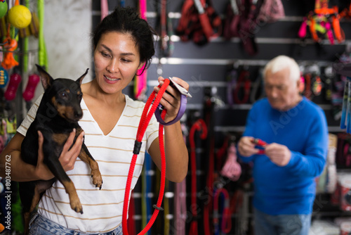 Positive asian woman choosing and buying leash for her doberman pinscher dog at a pet shop
