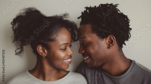 A candid waist-length perspective image featuring a couple smiling lovingly at each other against a plain background, their eyes filled with warmth and adoration as they share a mo
