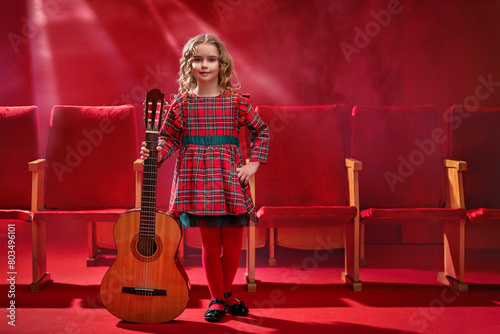 Little girl musician holds a guitar and smiles.