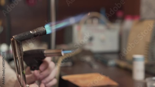 Jeweler lights a blowtorch and adjusts the flame in workshop. Hands close up. photo