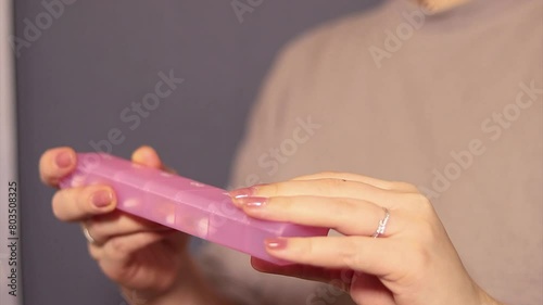 Close up of a woman taking a pill out of a pink pillbox, blurred background 