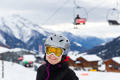 Young woman spending winter holidays in ski resort, posing in ski helmet and goggles outdoors with snow covered mountains in background photo