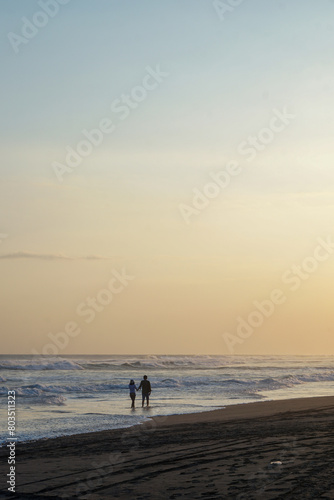 surfers walk along the beach as the sun sets