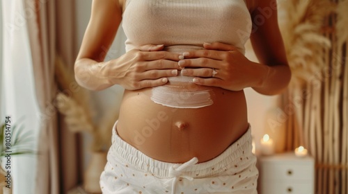 A close-up of a Caucasian woman hands applying stretch mark cream to her belly, in a softly lit, neutral-toned bathroom