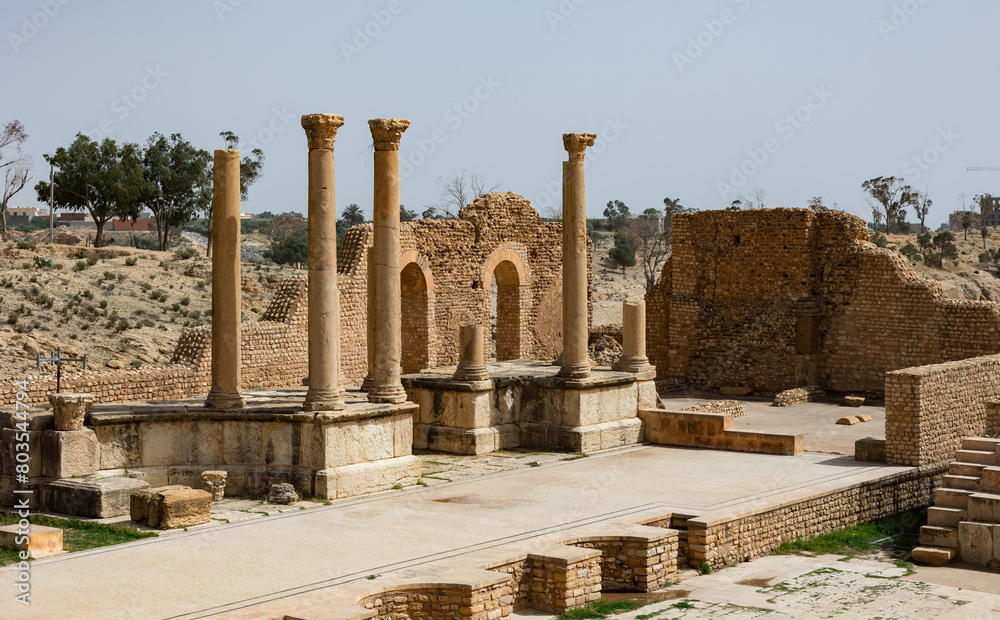 Obraz premium View of remains of ancient stone stage columns and seating steps of Roman theatre of Sufetula on sunny spring day. Historical archaeological sites of Tunisia..