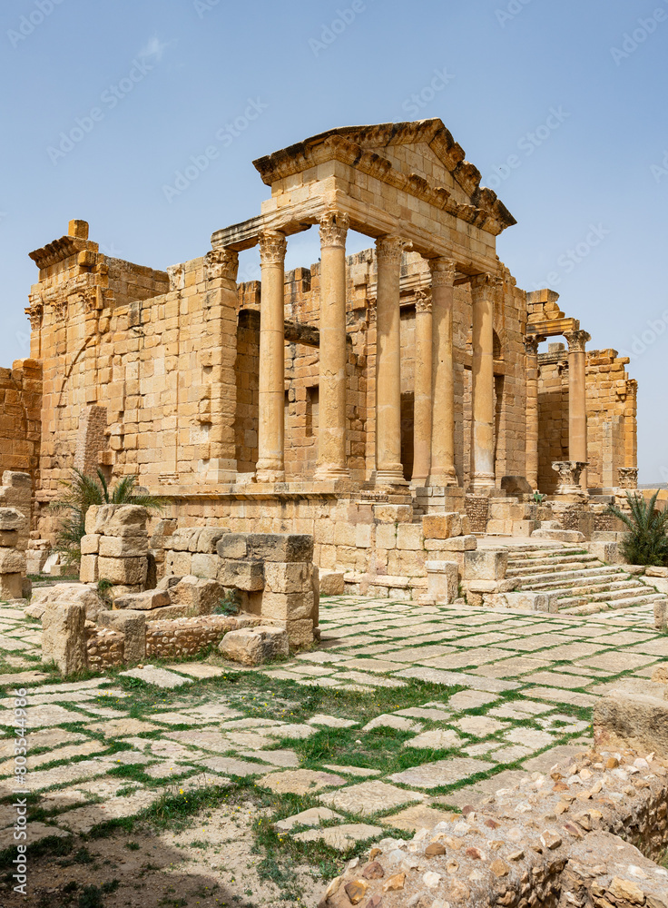 Fototapeta premium Scenic view of ancient Roman forum at Sbeitla archaeological site in Tunisia with majestical ruins of temple dedicated to Capitoline Triad - Jupiter, Juno, and Minerva on spring day