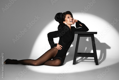 Beautiful woman in retro style in a black bodysuit and a bow in her hair in full length posing on a gray background. Beauty of body and face