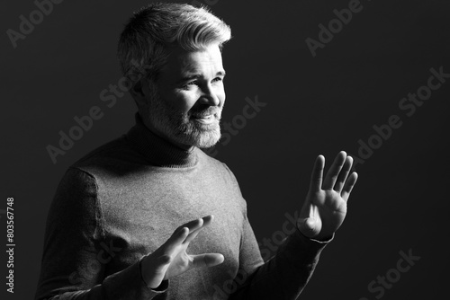 Portrait of smiling man gesturing on dark background. Black and white effect