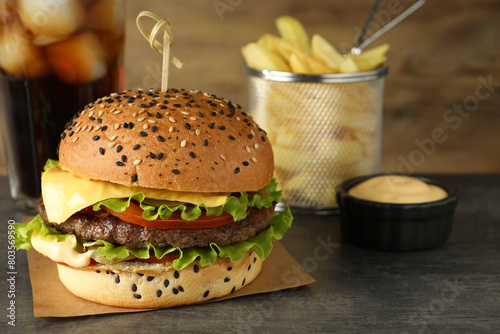 Burger with delicious patty, soda drink, french fries and sauce on gray table, closeup