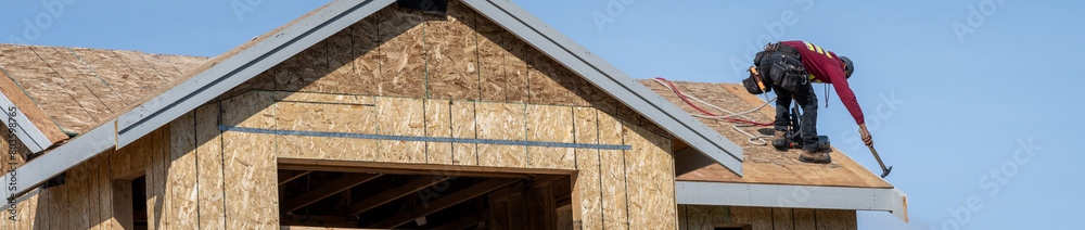 New home construction, minimalist image of new house shell with roofer working on roof, sunny blue sky spring day
New home construction, minimalist image of new house shell with roofer working on roof, sunny blue sky spring day