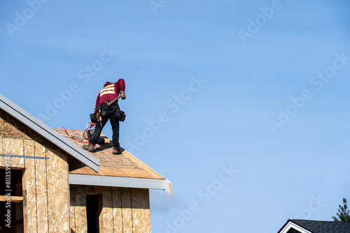 Workman with a nail gun working on roof of new home construction, minimalist image on a sunny spring day  © knelson20
