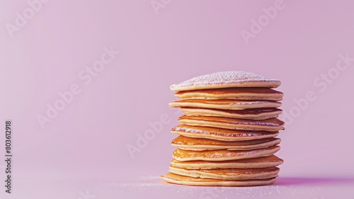 Stack of pancakes with powdered sugar on top against pink background photo