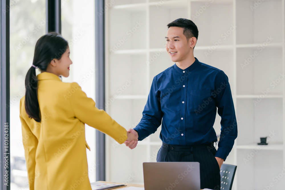 A man and a woman shake hands in a business setting A man and a woman shake hands in a business setting
