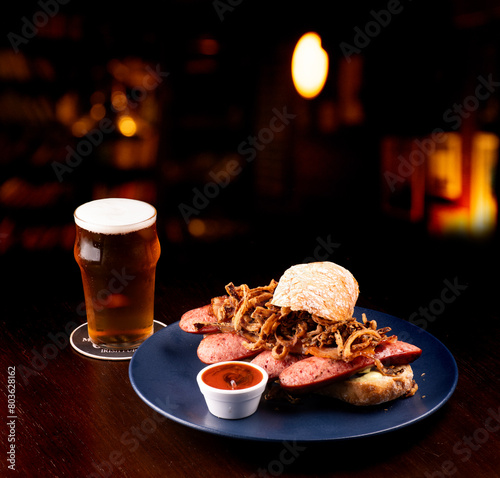 bock sausage sandwich with baguette crispy onion and pepper sauce paired with craft beer ale ipa apa blurred bar background