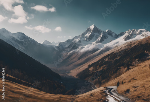 A breathtaking view of a mountain valley with snow-capped peaks and a winding path leading through golden hills under a moody sky. Mountain Day.