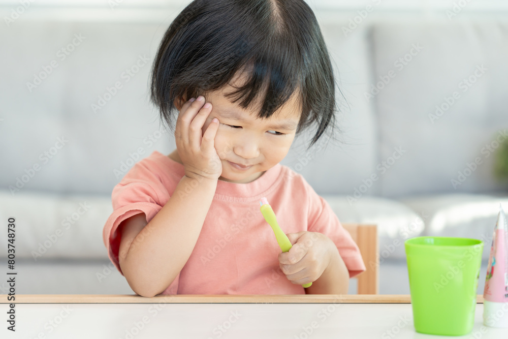 little asian girl presses hand to cheek, suffers from pain in tooth. Teeth decay, dental problems, child emotions and facial expression, oral health care, reducing sweets, fluorine coating little asian girl presses hand to cheek, suffers from pain in tooth. Teeth decay, dental problems, child emotions and facial expression, oral health care, reducing sweets, fluorine coating