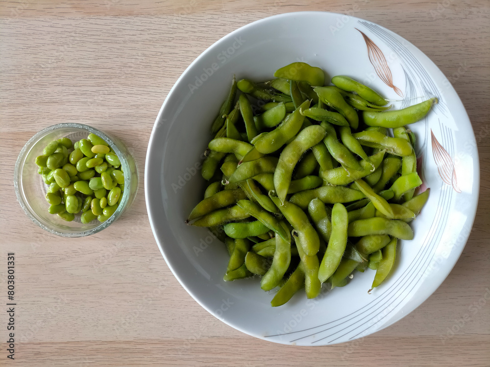 Freshly cooked green soybeans in bowls on a light brown wooden surface
Freshly cooked green soybeans in bowls on a light brown wooden surface