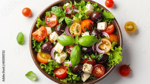Top view of fresh salad with tomatoes, mozzarella, olives, lettuce and basil in a wooden bowl on a white background.