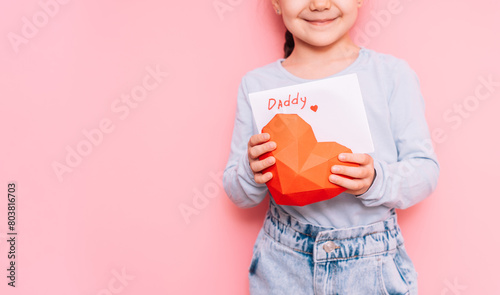 A little girl drew a card for dad on Father's Day in front of a pink background.