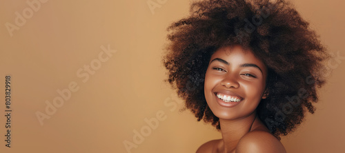 A black woman with an afro is smiling, her hair healthy and shiny, against a beige background.