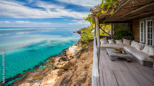 A stunning coastal scene featuring a cozy wooden deck perched atop a rugged cliff, offering a mesmerizing view of the clear turquoise waters lapping onto the rocky beach below.