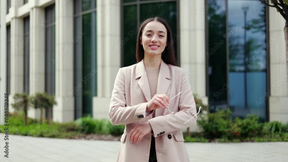 Successful female in elegant blazer and blouse taking off glasses and crossing arms while smiling outdoors. Positive woman feeling proud and looking at camera while standing on street in city center. Successful female in elegant blazer and blouse taking off glasses and crossing arms while smiling outdoors. Positive woman feeling proud and looking at camera while standing on street in city center.