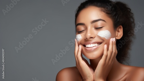 Beautiful young woman applying facial cream, her smile expressing pleasure and care for skin health