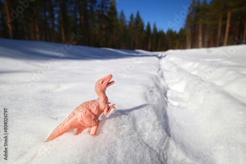 Toy dinosaur outside in the snow on sunny winter day