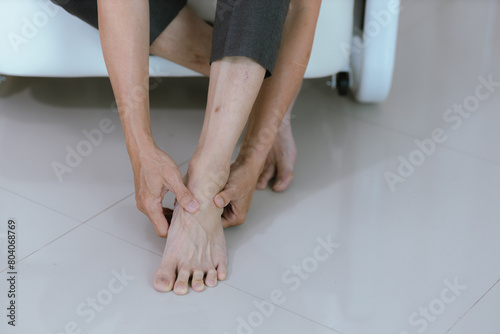 Close-up of an elderly man whose ankle hurts from walking too much. Massage painful feet and knees Calf pain sitting on the sofa at home