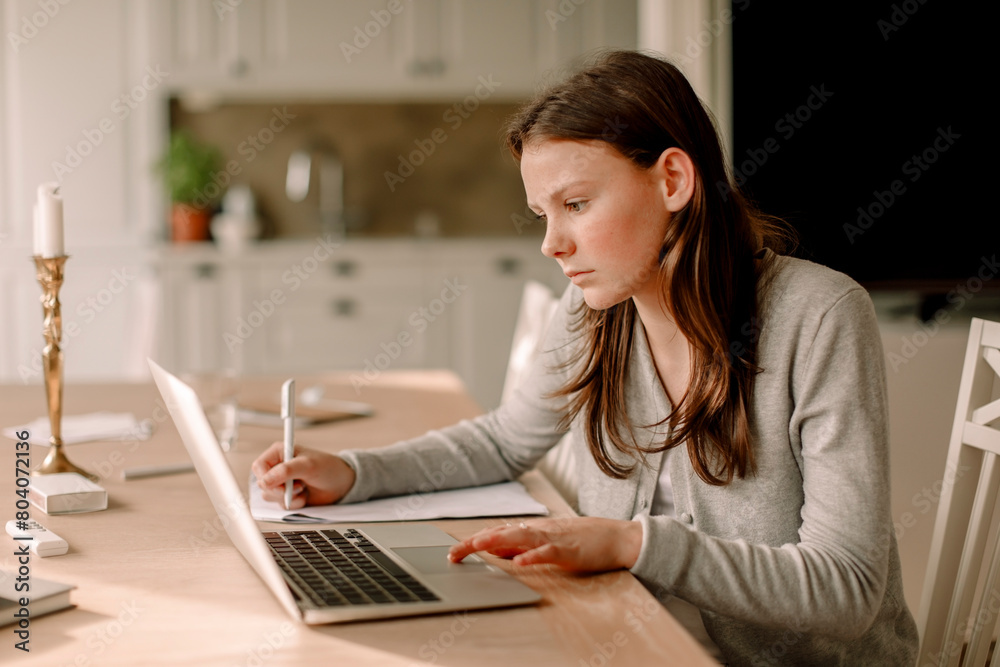 Teenage girl using laptop while studying at dining table in kitchen Teenage girl using laptop while studying at dining table in kitchen