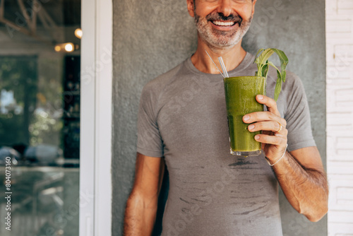 Midsection of smiling man holding glass of fresh green smoothie against wall at resort photo