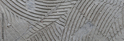 Panoramic image. Background of old grey tile adhesive on the floor. Abstract pattern of notched trowel