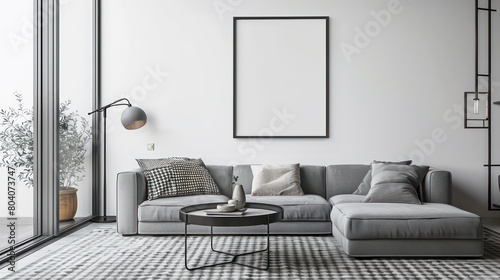 A mockup of an empty poster frame on the wall in a living room  with a sofa and coffee table nearby  on white walls and a carpeted floor  with a lamp stand  a light grey couch with beige cushion.