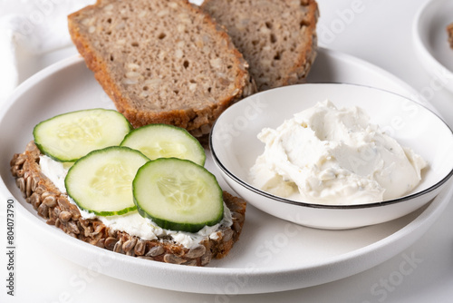 Rye bread with cream cheese and cucumbers on a white table. Whole grain rye bread with seeds