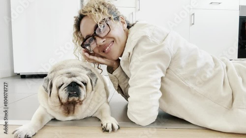 One adult woman alone at home relaxing on the floor with her best friend dog enjoying cuddle and fun with old pug companion. Animal canine relationship domestic real lifestyle female people photo