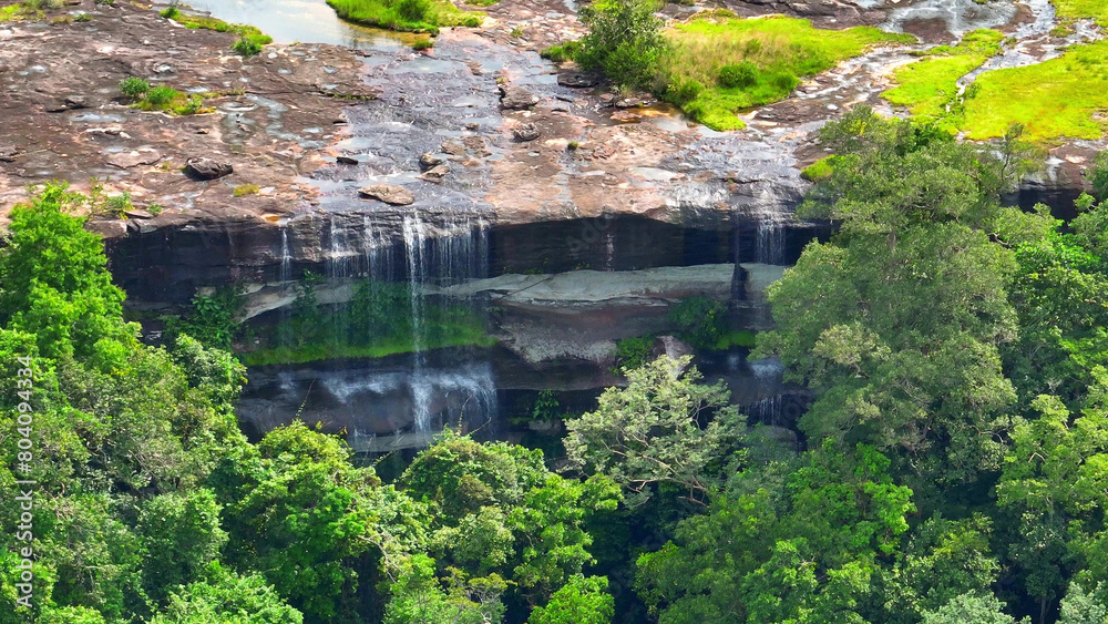 Nature's Masterpiece: An awe-inspiring waterfall plunging from great heights, embraced by a lush, verdant rainforest, a true natural wonder. Pha Taem National Park, Ubon Ratchathani Province, Thailand