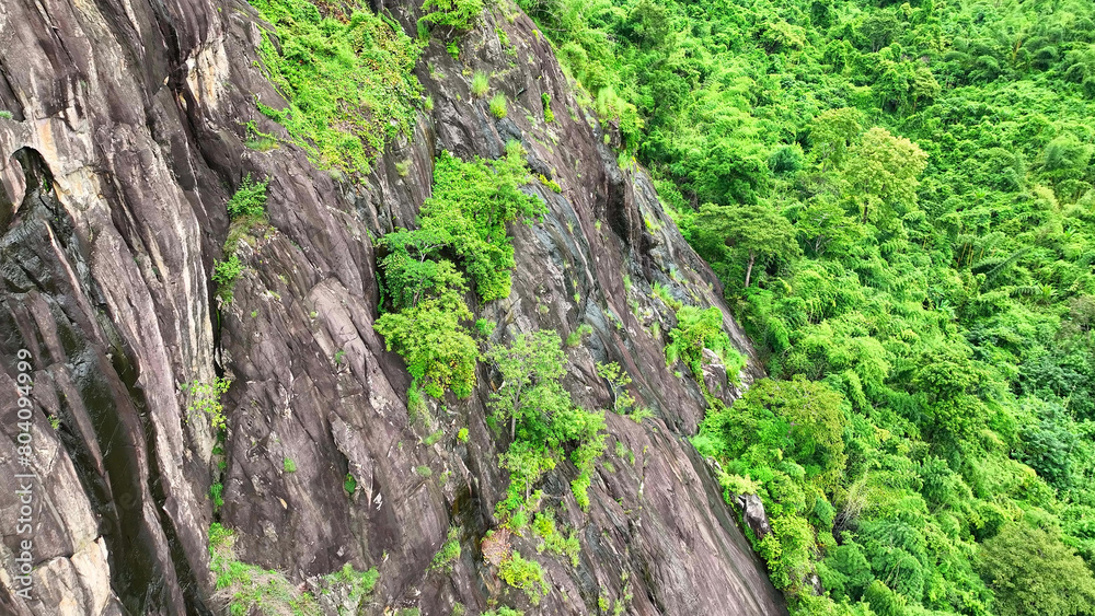 Drone captures rocky cliffs encircled by vibrant tropical rainforest, showcasing the raw beauty of nature's contrast, a breathtaking spectacle. Thailand.
