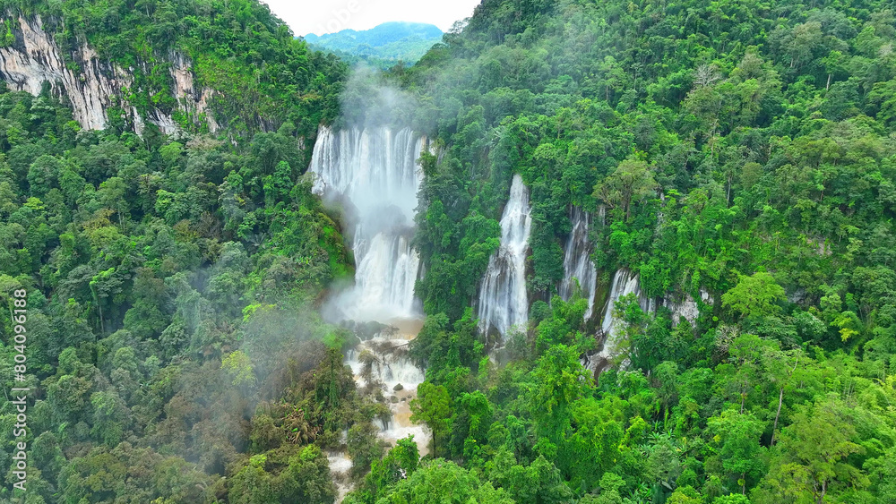 A hidden gem in the lush tropical rainforest, the grand waterfall cascades through a dense green forest canopy, revealed by a mesmerizing drone's view. Untamed woods: Life's green home. Thailand.

