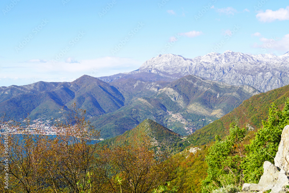 Contrasting landscape as the seasons change: autumn colors of Mount Vrmac and winter Orjen in the background (Montenegro). View of the hill with the Church of St. Vitus in the Bay of Kotor. Contrasting landscape as the seasons change: autumn colors of Mount Vrmac and winter Orjen in the background (Montenegro). View of the hill with the Church of St. Vitus in the Bay of Kotor.