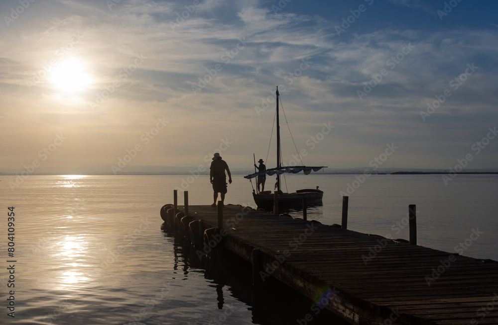 A fishing boat arrives at the pier of the Albufera lake port at sunset