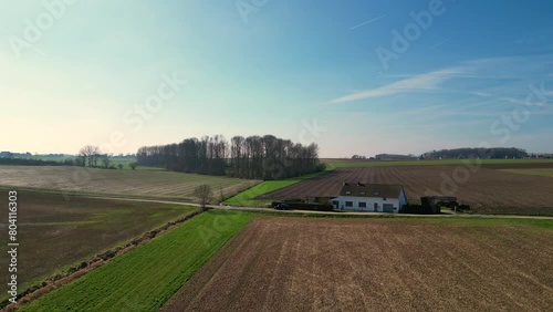 This serene stock footage offers a sweeping aerial panorama of the tranquil farmlands of Pajottenland. The expansive agricultural fields, patchworked with varying shades of green and brown, symbolize photo