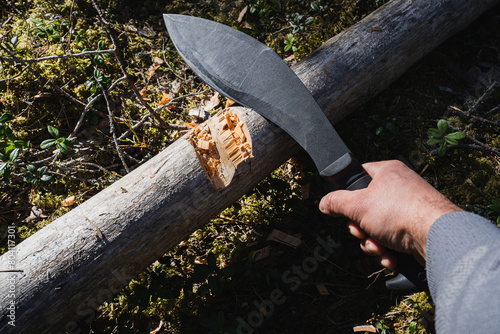 A large black tactical kukri knife for chopping wood in a man's hand in the forest. photo