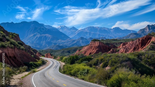 Road winds through canyon with mountains in background under blue sky