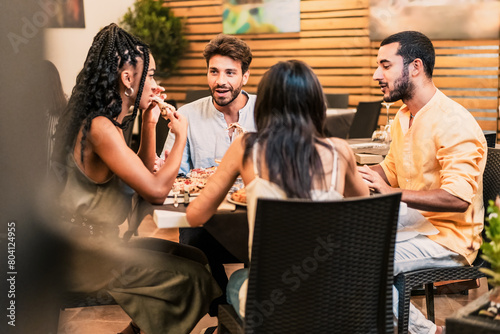 Diverse group of friends - enjoying dinner and conversation at a restaurant, sharing a meal in a lively urban setting - social, fun. © Lomb