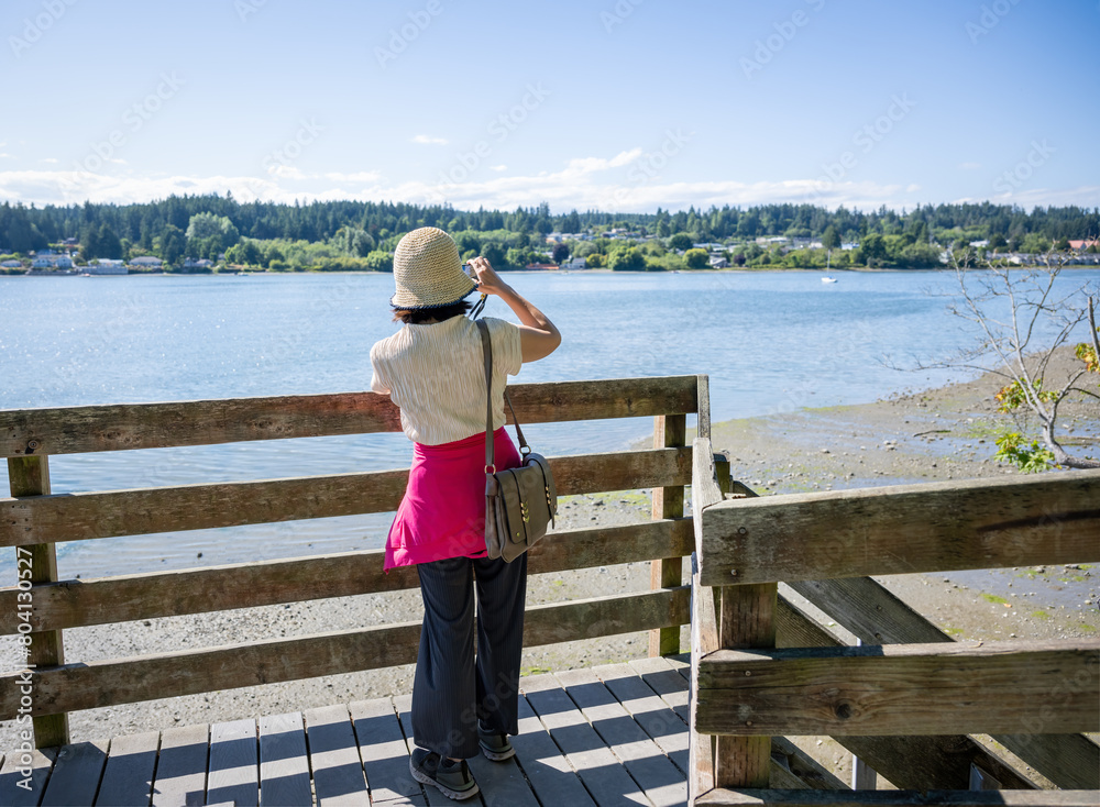 Woman taking photos using a smartphone on the bridge in Poulsbo. Poulsbo is a city on Liberty Bay in Kitsap County, Washington State.