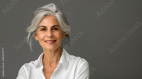 Stylish senior woman with grey hair in a white shirt smiling and looking at the camera , grey background photo