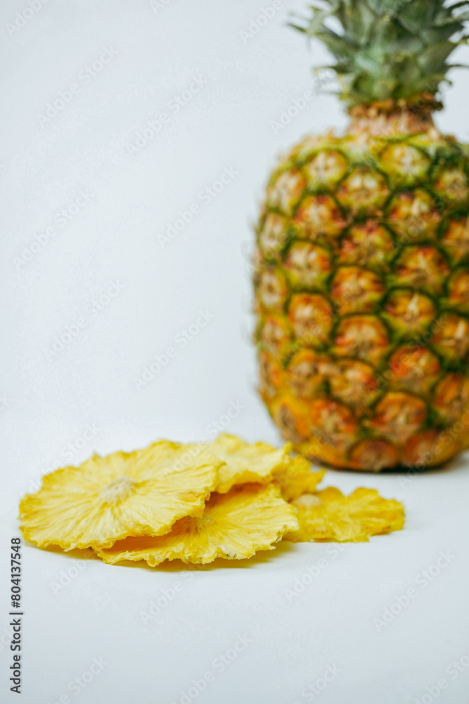 Vibrant yellow dried pineapple pieces in the foreground, with a whole pineapple blurred in the background, perfect for health snacks Vibrant yellow dried pineapple pieces in the foreground, with a whole pineapple blurred in the background, perfect for health snacks