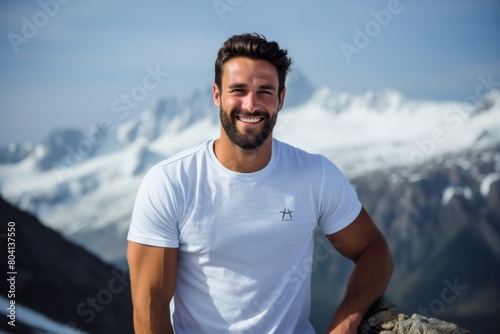 Portrait of a blissful man in his 30s dressed in a casual t-shirt while standing against snowy mountain range