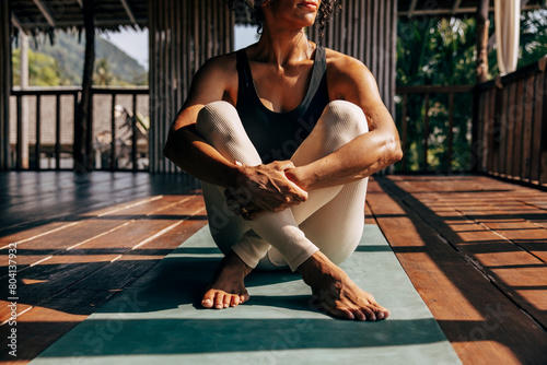 Low section of woman hugging knees while sitting on yoga mat at wellness resort photo