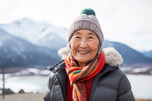 Portrait of a smiling asian woman in her 80s sporting a trendy beanie on snowy mountain range